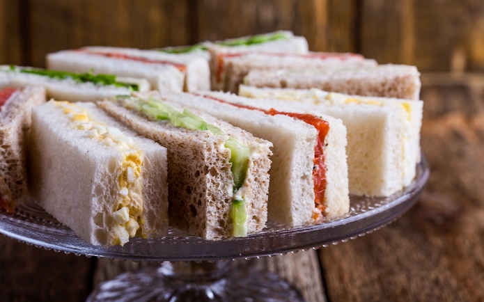 English tea sandwiches with various fillings on a glass cake stand.