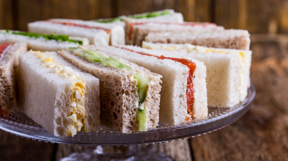 English tea sandwiches with various fillings on a glass cake stand.