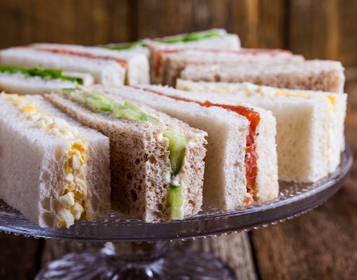 English tea sandwiches with various fillings on a glass cake stand.