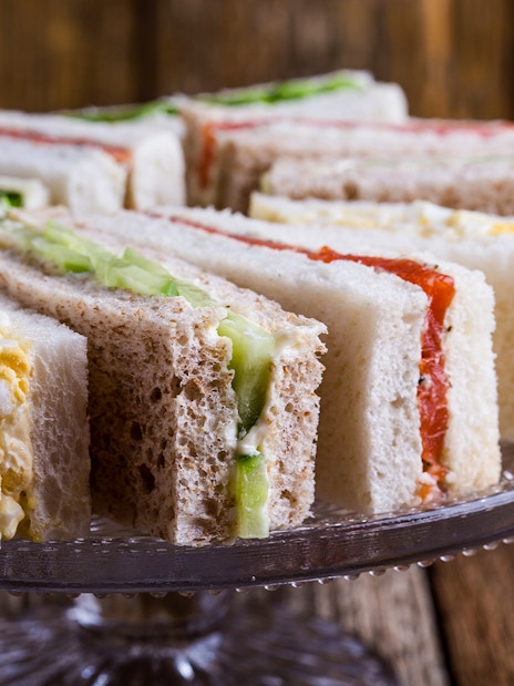 English tea sandwiches with various fillings on a glass cake stand.