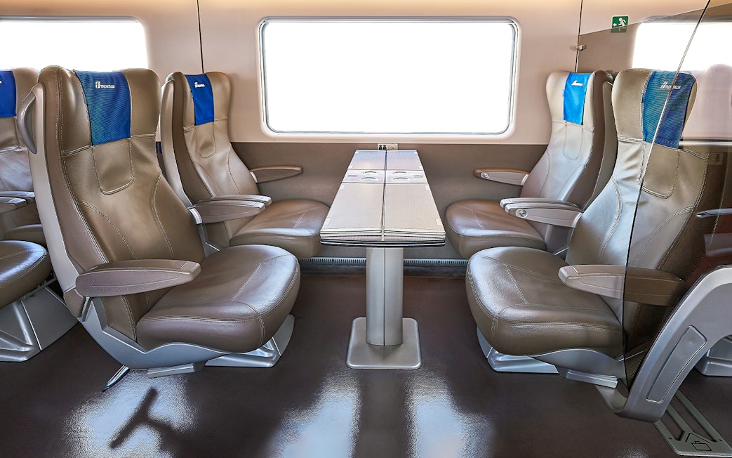 Trenitalia business class seats with table in train interior.
