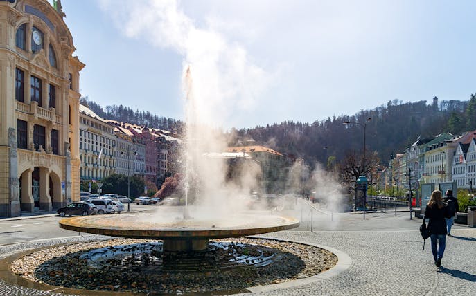 Fountain in Karlovy Vary town square with historic buildings, Czech Republic.