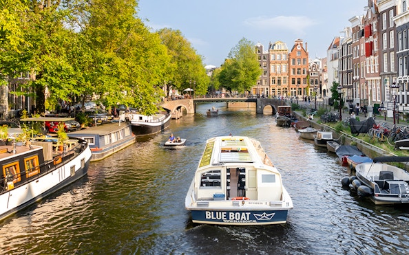 Canal cruise boat on Amsterdam's scenic canal with historic buildings and trees.