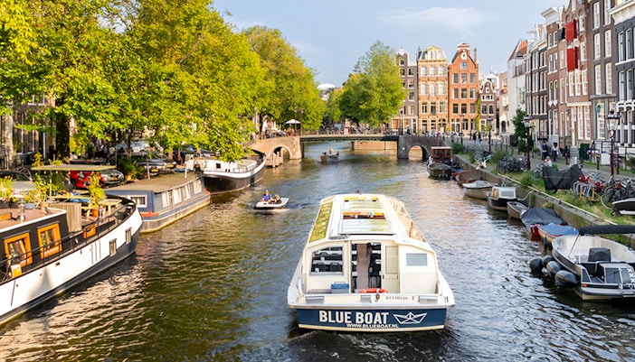 Canal cruise boat on Amsterdam's scenic canal with historic buildings and trees.