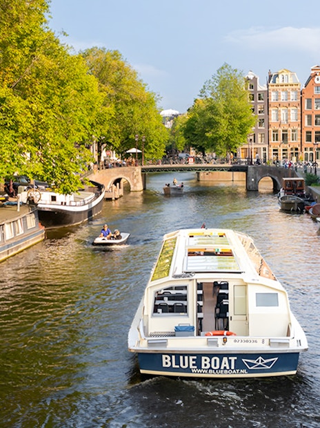 Canal cruise boat on Amsterdam's scenic canal with historic buildings and trees.