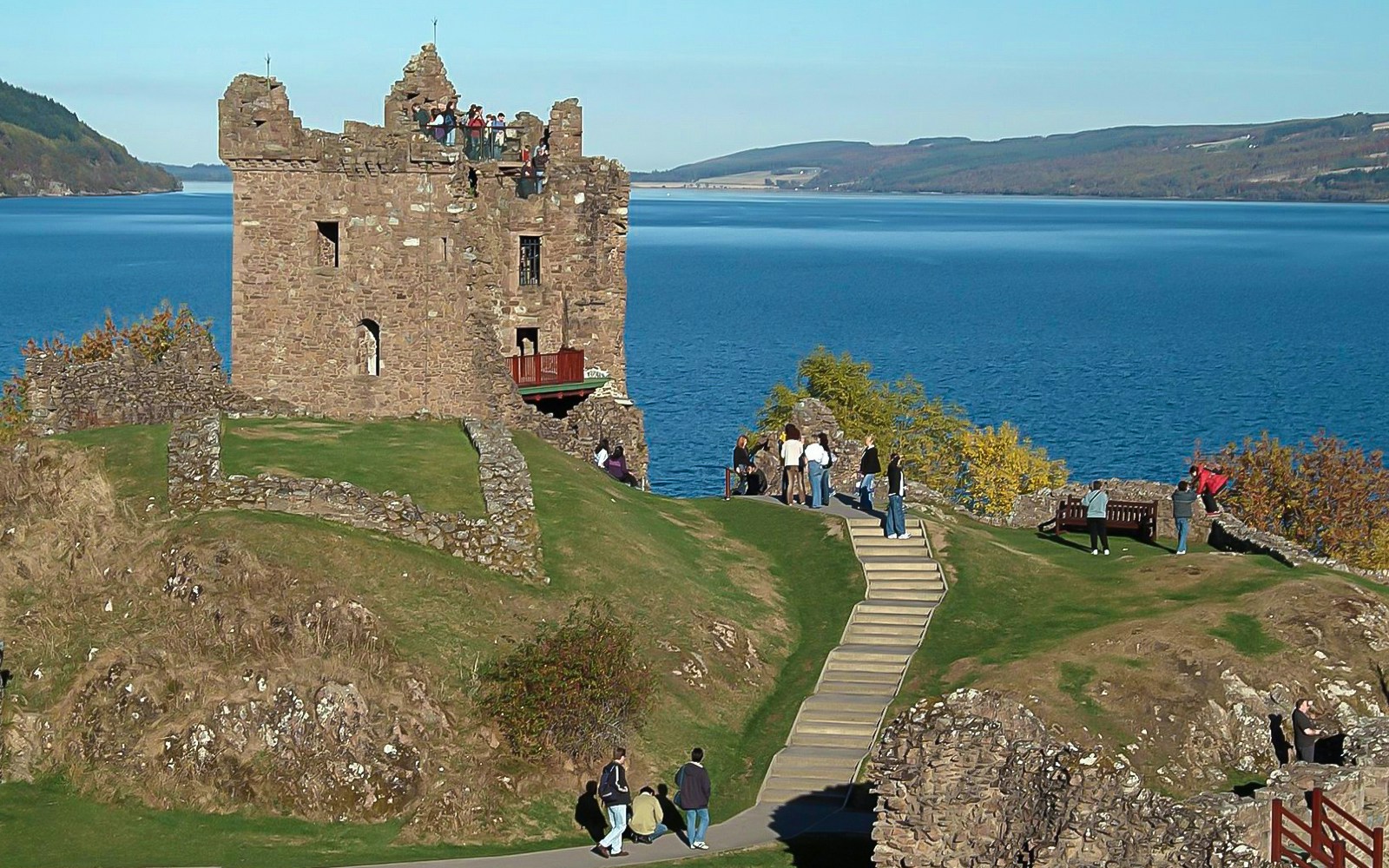Urquhart Castle overlooking Loch Ness with tourists exploring the grounds.