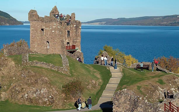 Urquhart Castle overlooking Loch Ness with tourists exploring the grounds.