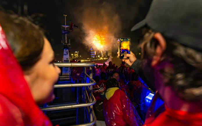 Tourists on a boat at Niagara Falls watching fireworks at night.
