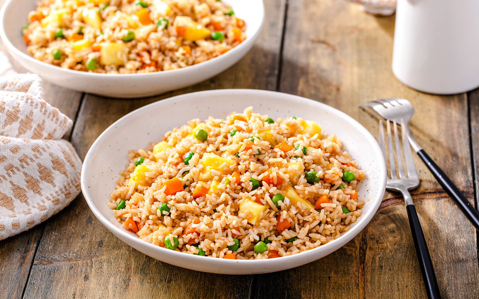 Pineapple fried rice with peas and carrots in a white bowl on a wooden table.