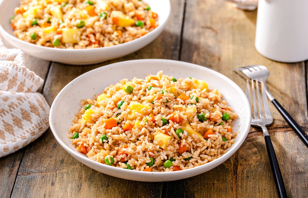 Pineapple fried rice with peas and carrots in a white bowl on a wooden table.