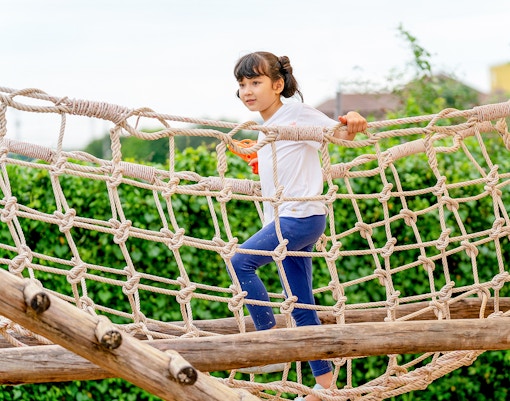 Child climbing rope bridge at outdoor adventure park.