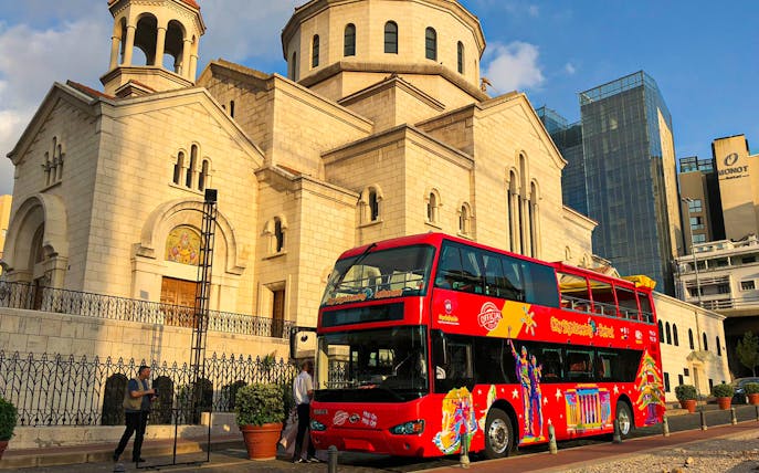 Red double-decker bus in front of a historic church on Beirut Hop On Hop Off tour.