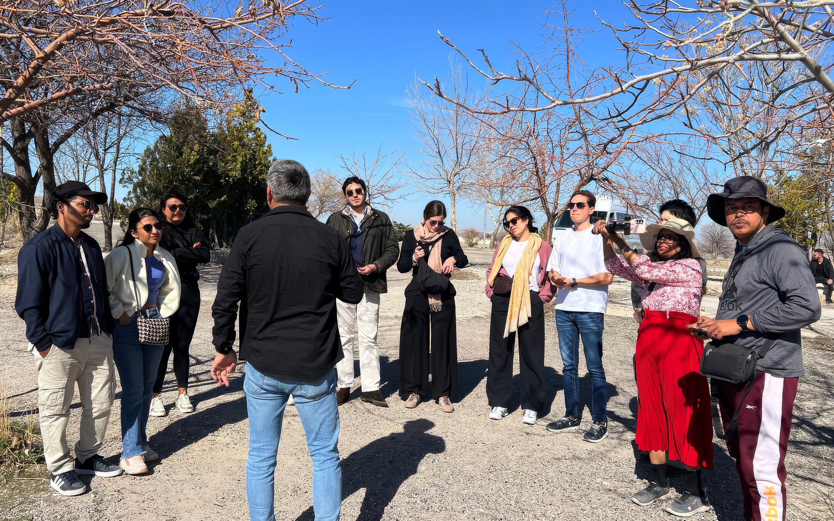 Guide speaking to a group of tourists outdoors under bare trees.
