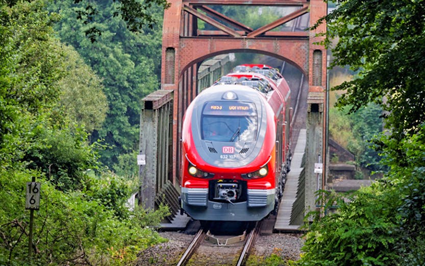 Red train crossing a bridge in a lush forest, Germany, showcasing the Interrail Pass experience.