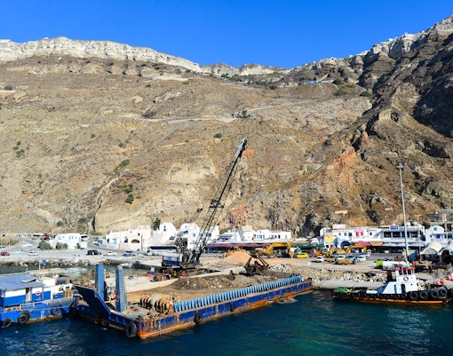 Athinios Port with docked boats and construction equipment, Santorini Volcano backdrop.