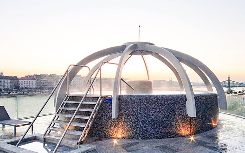 Rooftop pool at Rudas Bath in Budapest with city skyline in the background.