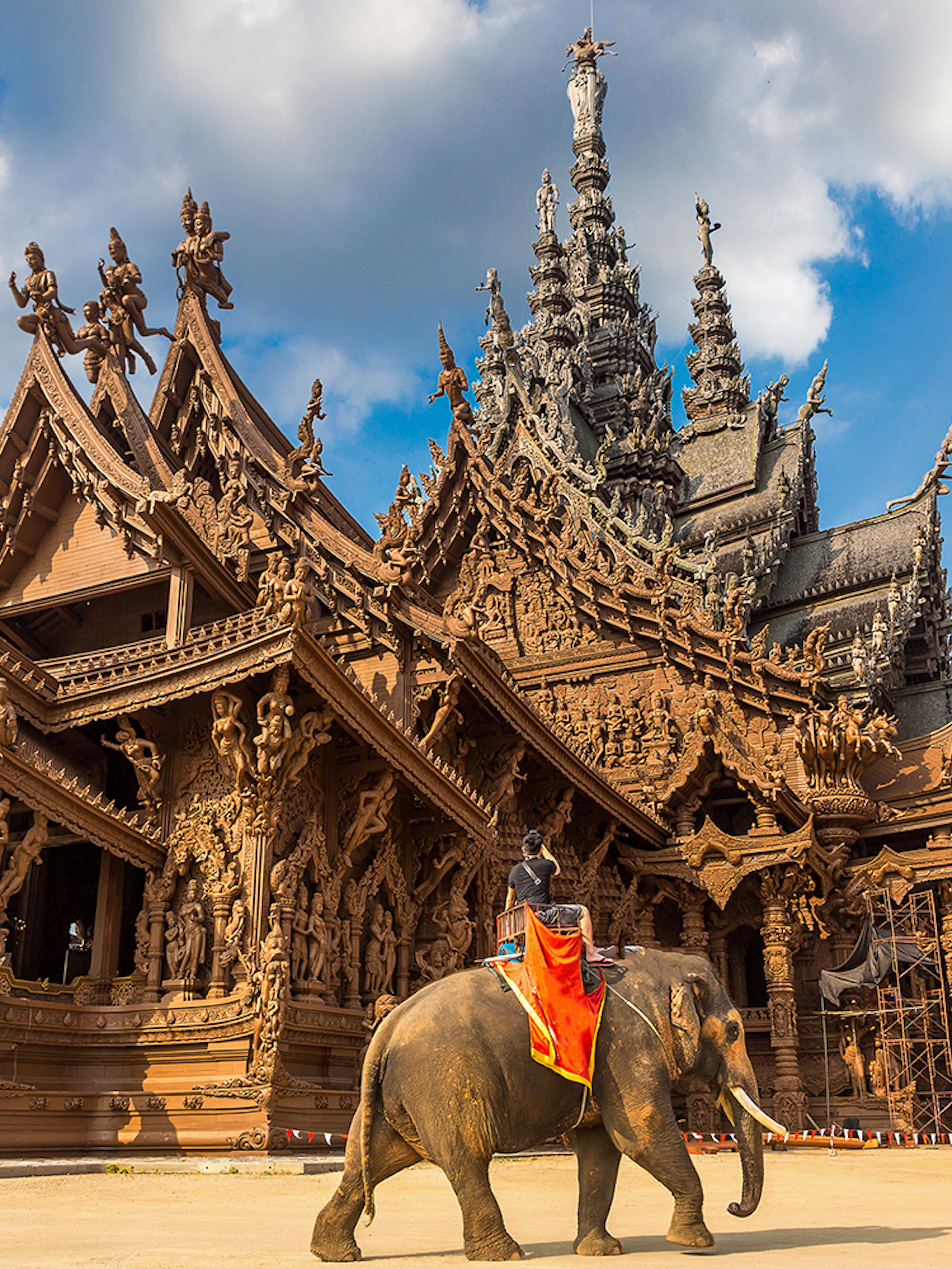Sanctuary of Truth in Pattaya with intricate wooden carvings and an elephant in the foreground.