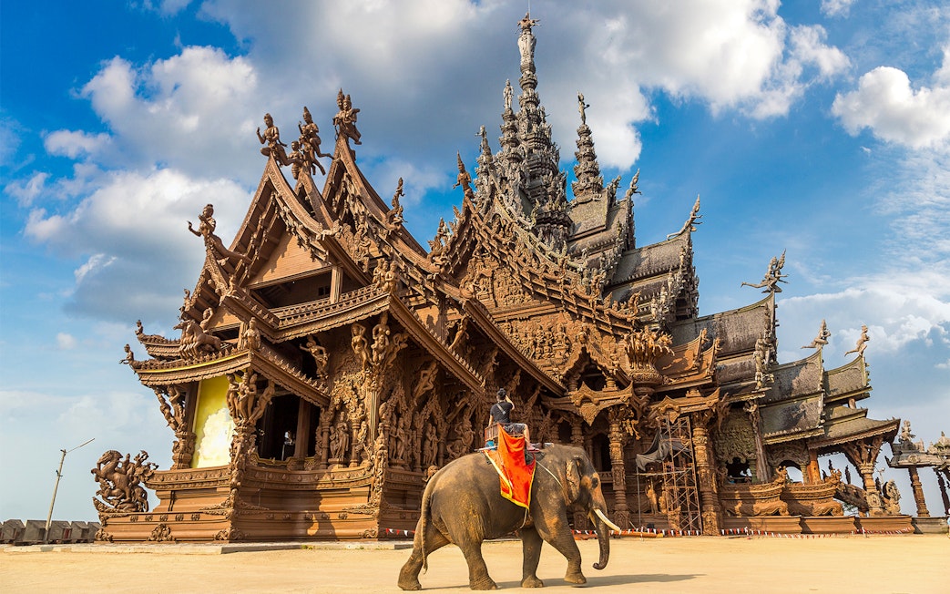 Sanctuary of Truth in Pattaya with intricate wooden carvings and an elephant in the foreground.