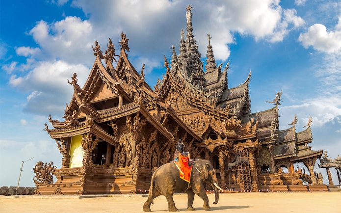 Sanctuary of Truth in Pattaya with intricate wooden carvings and an elephant in the foreground.