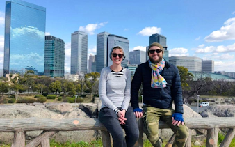 Couple resting during Osaka Castle bike tour with city skyline in background.
