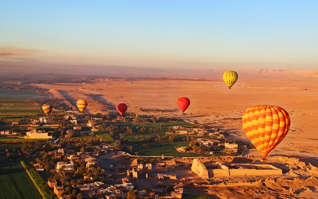 Hot air balloons over Luxor landscape with ancient ruins and fields.