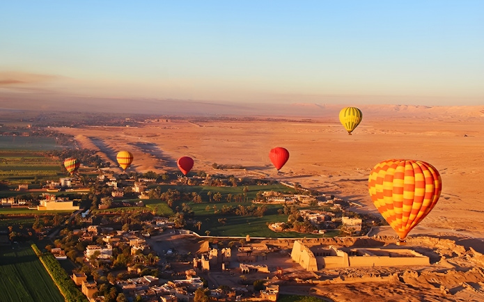 Hot air balloons over Luxor landscape with ancient ruins and fields.