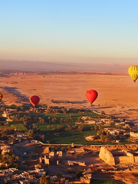 Hot air balloons over Luxor landscape with ancient ruins and fields.