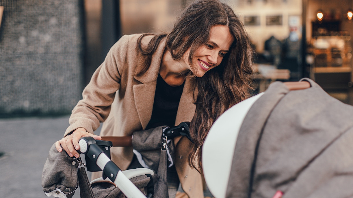 Young mother smiling at stroller in urban setting.
