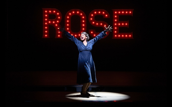Performer on stage with "Rose" sign in lights, related to Gypsy musical.