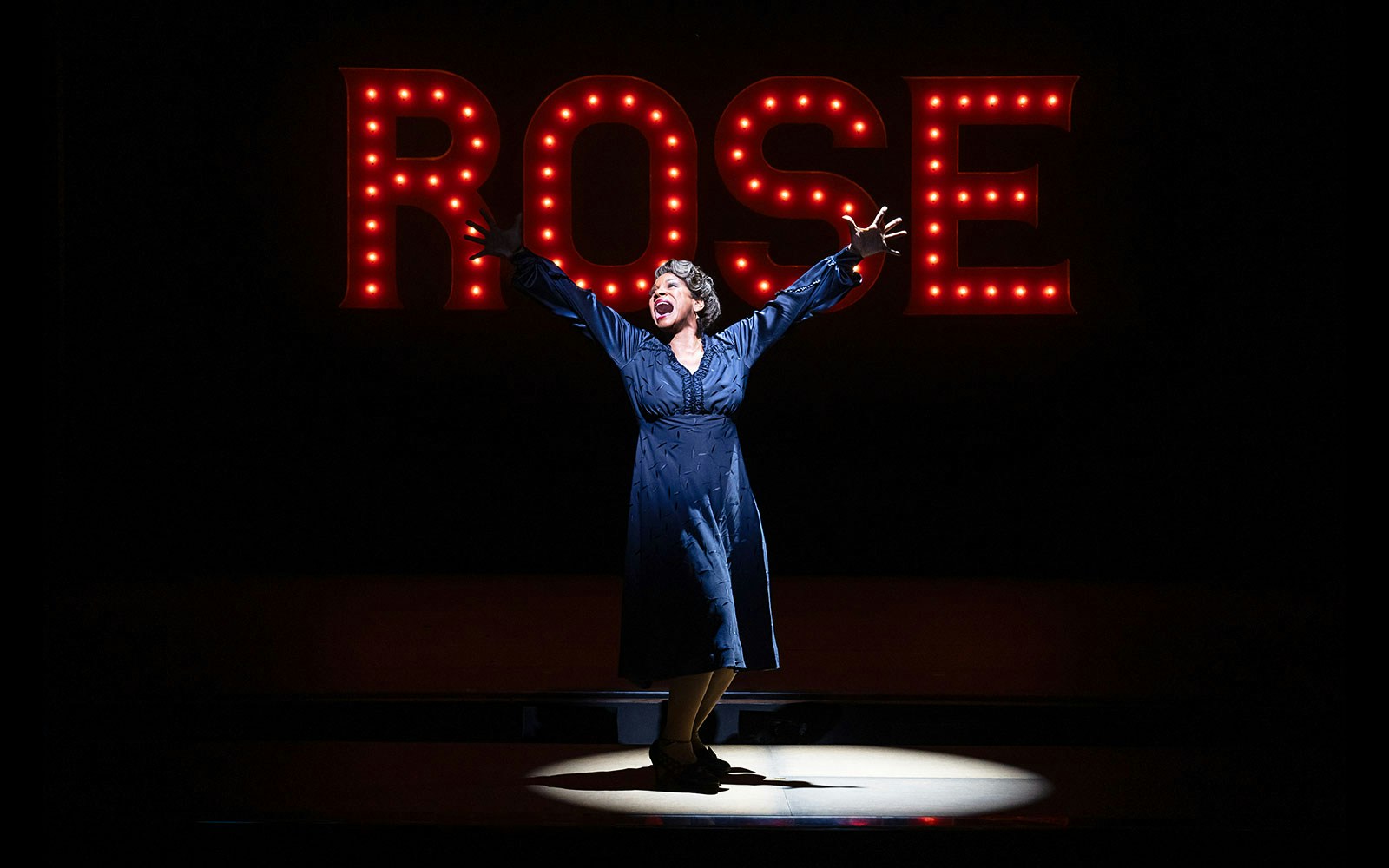 Performer on stage with "Rose" sign in lights, related to Gypsy musical.