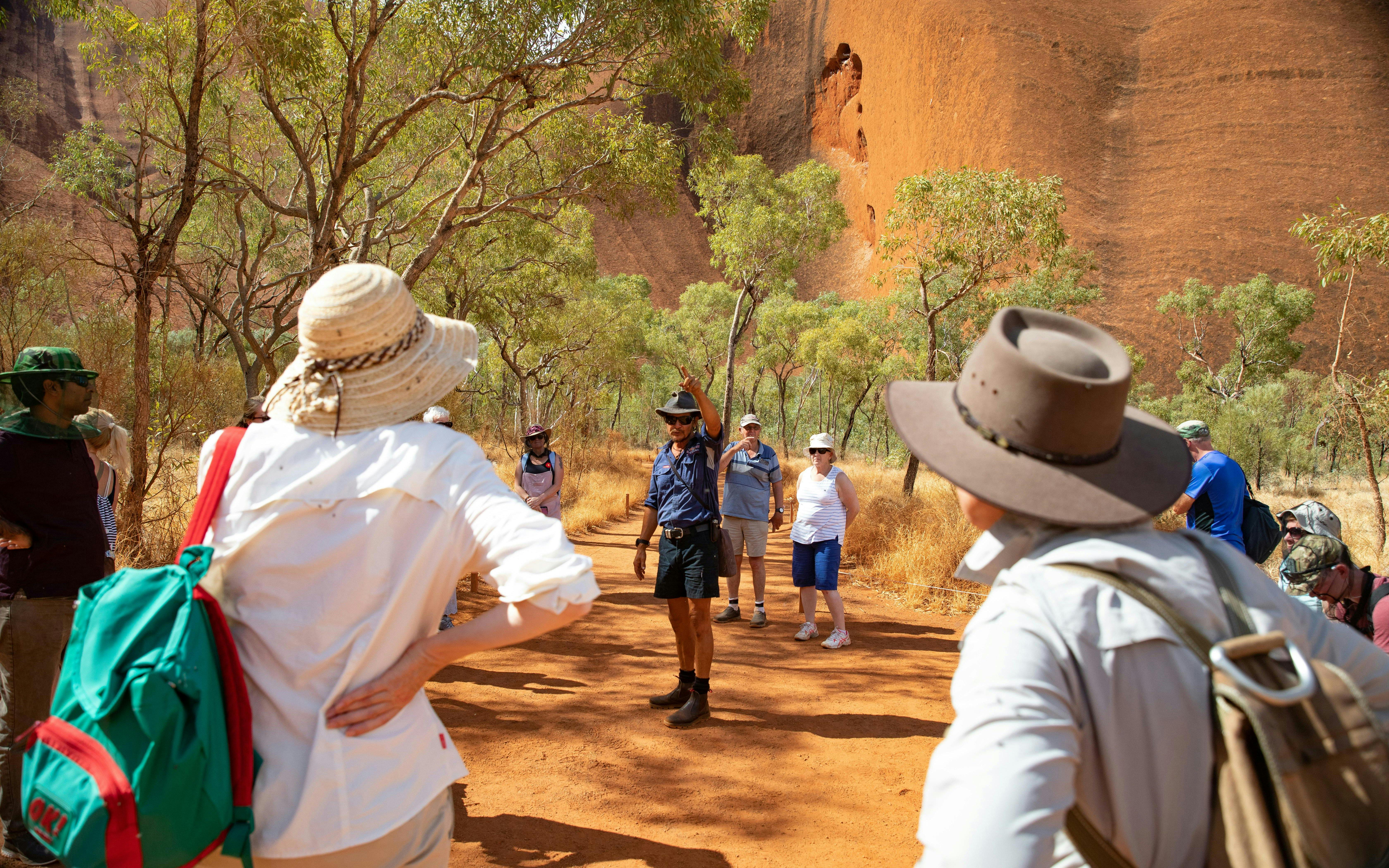 Tour group exploring Uluru with guide, surrounded by trees and red rock formations in Alice Springs.