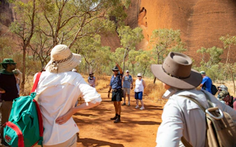 Tour group exploring Uluru with guide, surrounded by trees and red rock formations in Alice Springs.