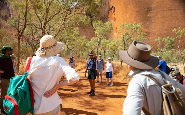 Tour group exploring Uluru with guide, surrounded by trees and red rock formations in Alice Springs.