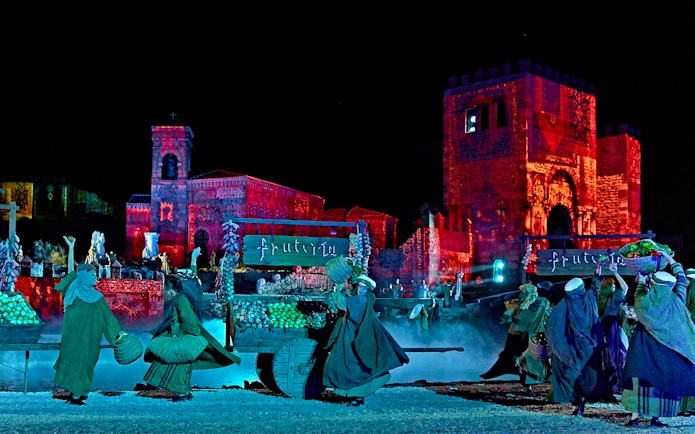 Performers in historical costumes during The Dream of Toledo night show, with illuminated medieval buildings.
