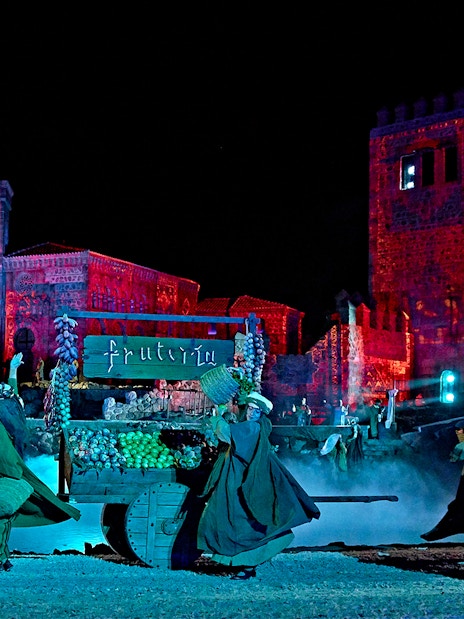 Performers in historical costumes during The Dream of Toledo night show, with illuminated medieval buildings.