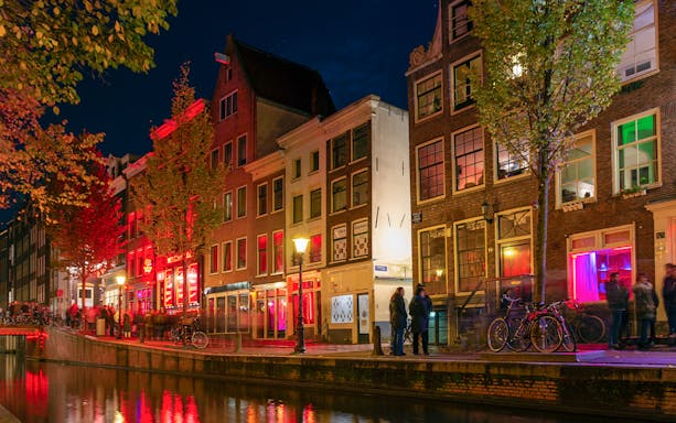 Evening view of Amsterdam's Red-Light District with illuminated canal and historic buildings.