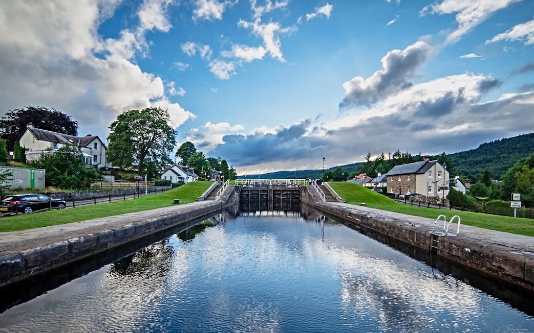 Canal lock at Fort Augustus with surrounding houses and greenery under a blue sky.