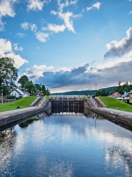 Canal lock at Fort Augustus with surrounding houses and greenery under a blue sky.