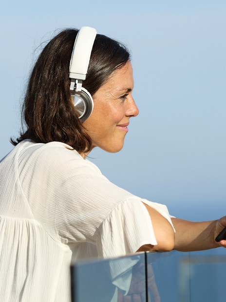 Woman listening to audio guide on cruise deck with ocean view.