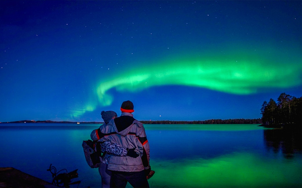 Couple watching Northern Lights over a lake in Rovaniemi, Finland.