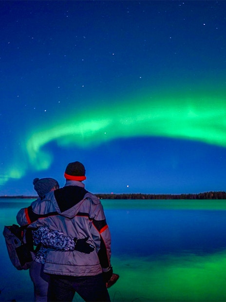 Couple watching Northern Lights over a lake in Rovaniemi, Finland.