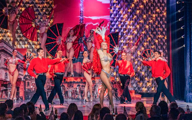Performers on stage at Cabaret La Nouvelle Eve, Paris, with dancers in vibrant costumes.