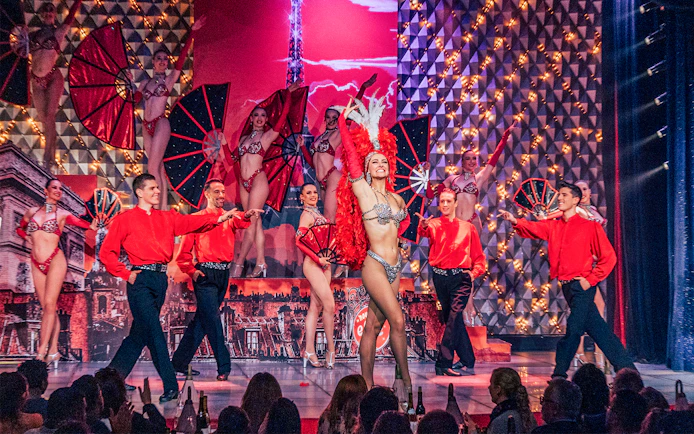 Performers on stage at Cabaret La Nouvelle Eve, Paris, with dancers in vibrant costumes.