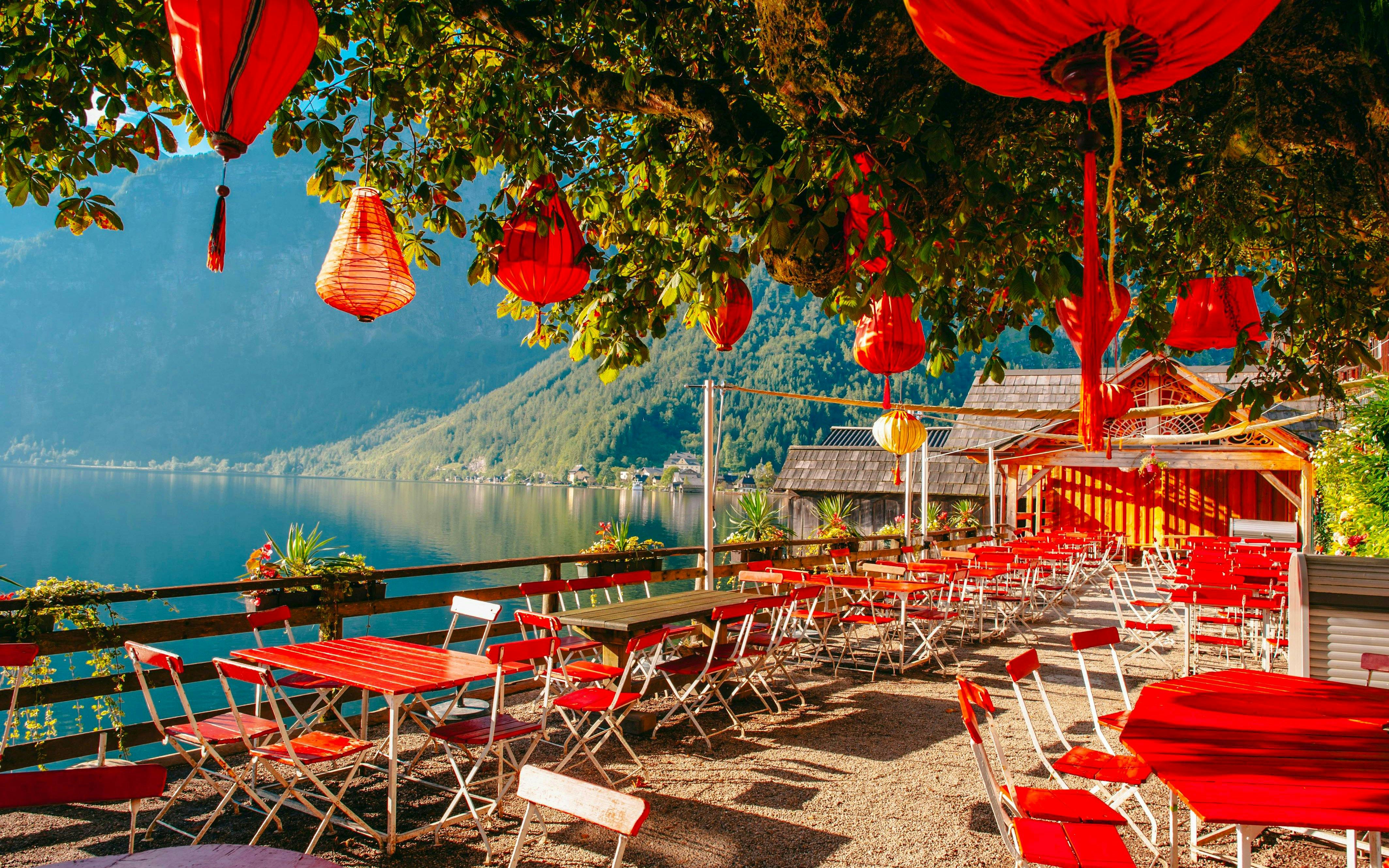 Lakeside cafe with red lanterns and chairs overlooking Hallstatt lake, Austria.