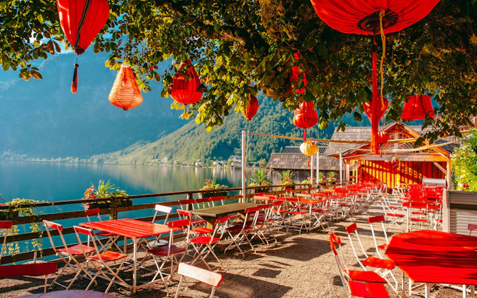Lakeside cafe with red lanterns and chairs overlooking Hallstatt lake, Austria.