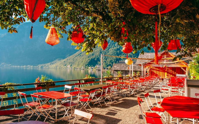 Lakeside cafe with red lanterns and chairs overlooking Hallstatt lake, Austria.