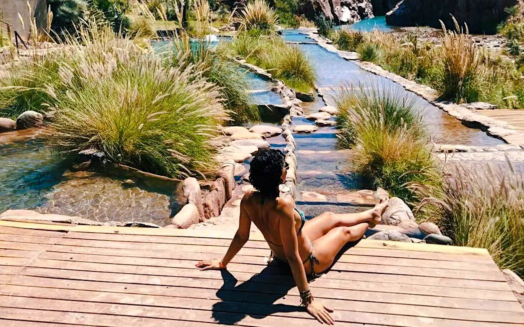 Guests relaxing by natural thermal pools at Cacheuta Spa, surrounded by lush greenery.