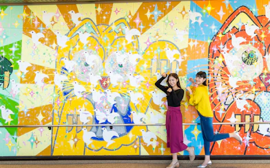 Colorful mural with doves at Hiroshima Orizuru Tower, featuring two people posing playfully.