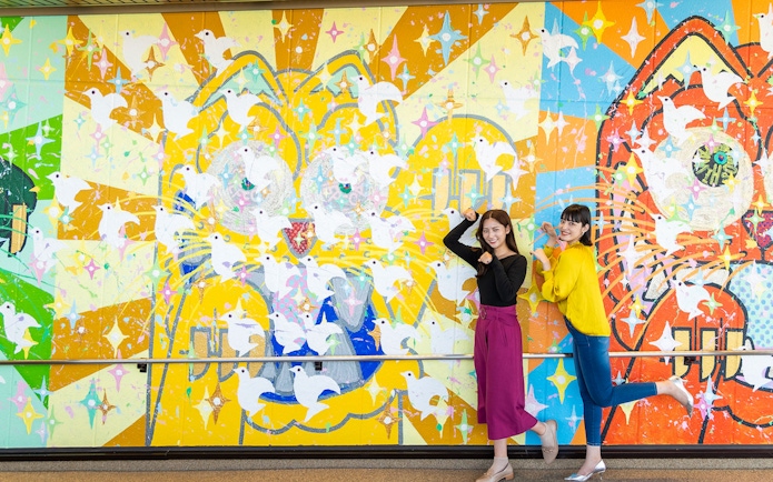 Colorful mural with doves at Hiroshima Orizuru Tower, featuring two people posing playfully.