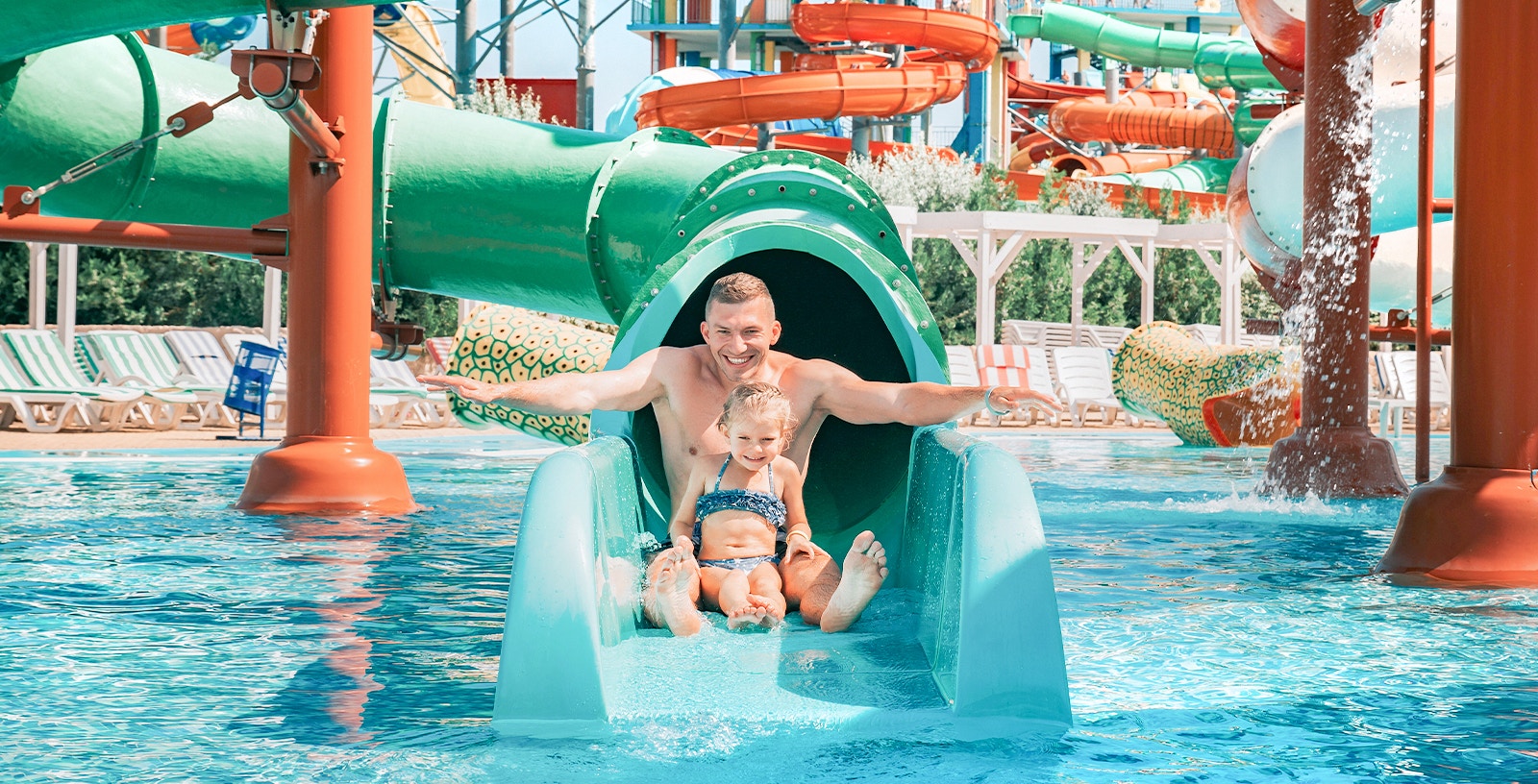 Father and daughter sliding down water slide at a colorful water park.